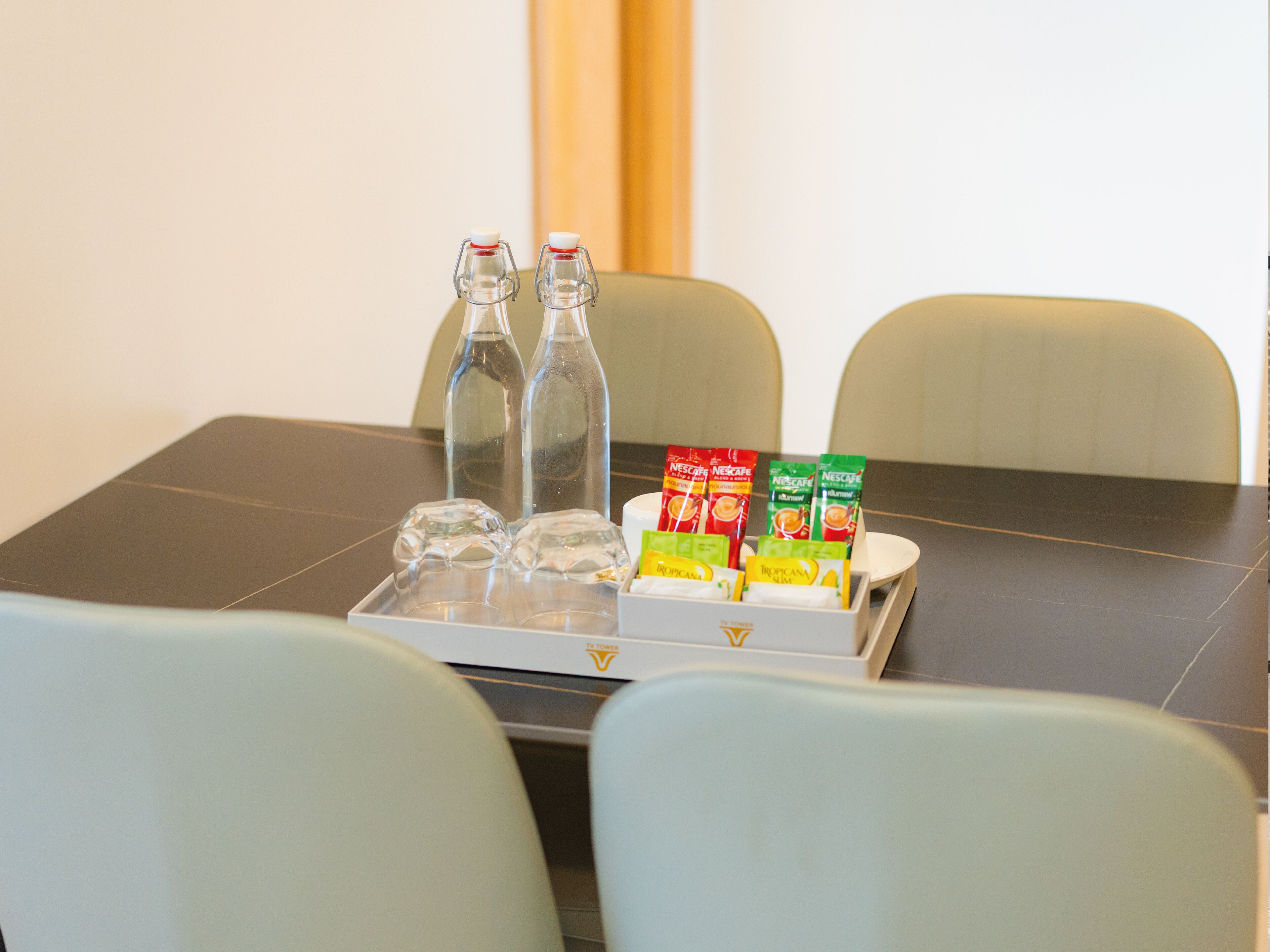 A table with two clear bottles, a tray with water glasses and Nescafé instant coffee packets.
