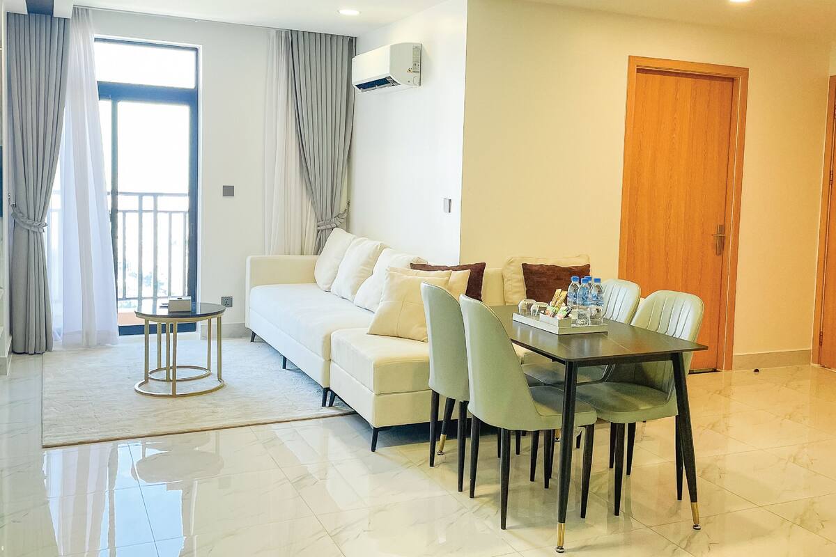 A modern living room with a sofa, dining table, chairs, and a balcony with curtains.