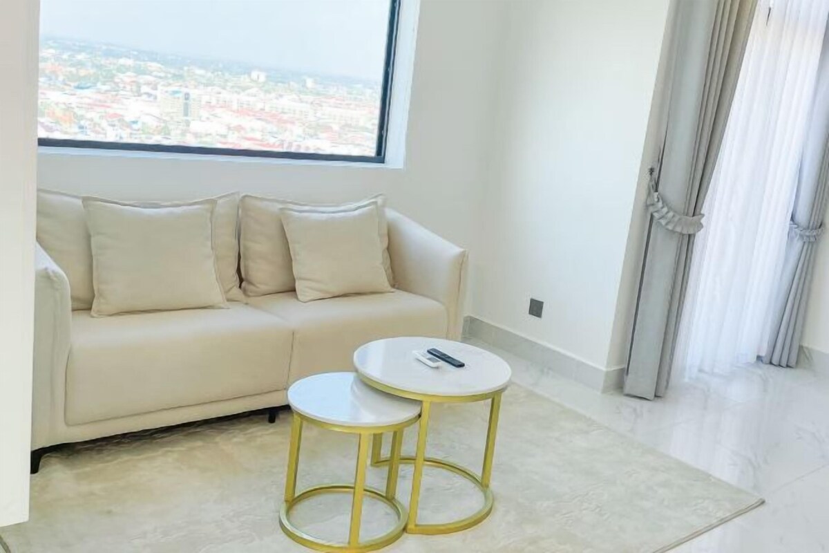 A modern living room with a sofa, two small round tables, and a view of a cityscape through a large window.
