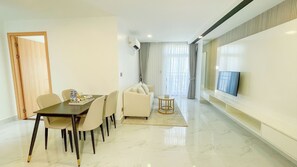 A modern living room with a dining area, a sofa, a TV mounted on the wall, and a wooden door. - TV-Tower 1 (Phnom Penh)