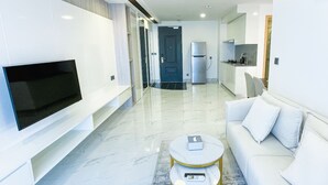 Un salón moderno con televisor de pantalla plana, un sofá, una mesa de centro y una cocina al fondo.