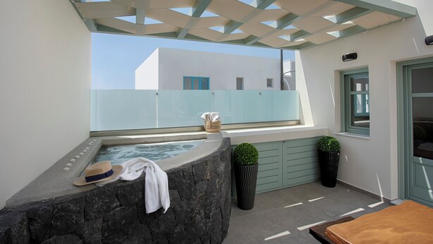A rooftop terrace with a stone jacuzzi, a sunshade, and a potted plant. - Katerina Villas 11 12 13 & 3PriveJacuzzi (Santorini)