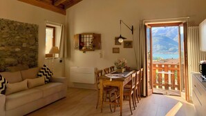 A cozy living room with a wooden ceiling, stone wall, and a view of mountains through the open door. - Alle Macine - Molino Maufet (Colico)