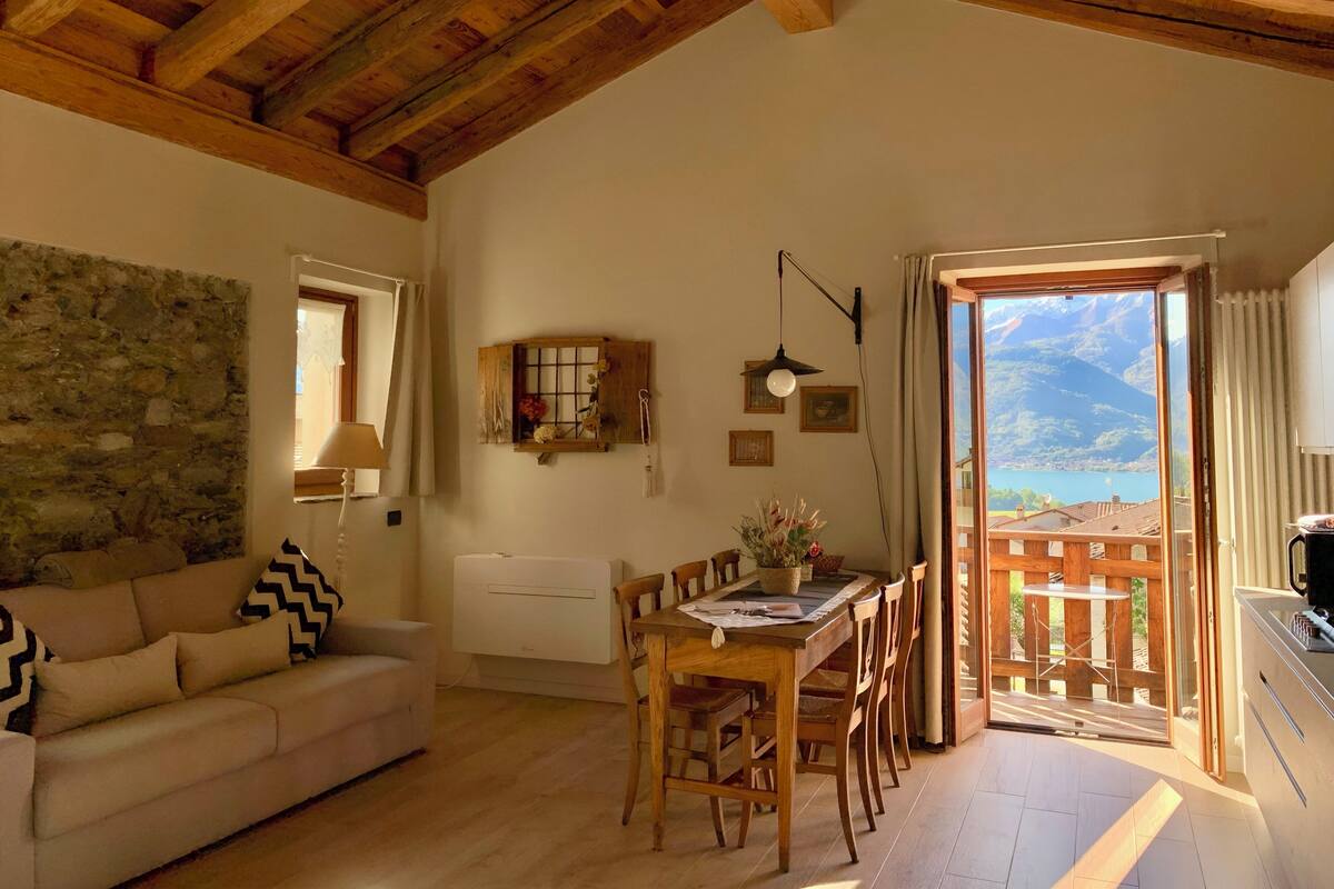 Uma sala de estar aconchegante com teto de madeira, parede de pedra e vista para as montanhas pela porta aberta.