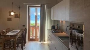 A modern kitchen with wooden beams, a dining area with a table and chairs, and a view through a glass door. - Alle Macine - Molino Maufet (Colico)
