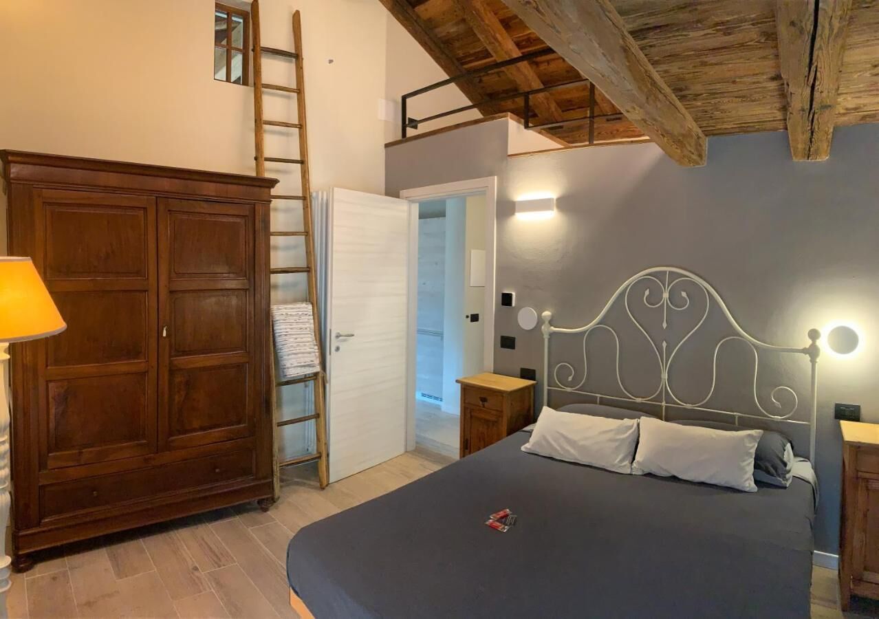 Une chambre avec une grande armoire, un lit avec une tête de lit en métal, des tables de chevet et une échelle menant à une mezzanine.