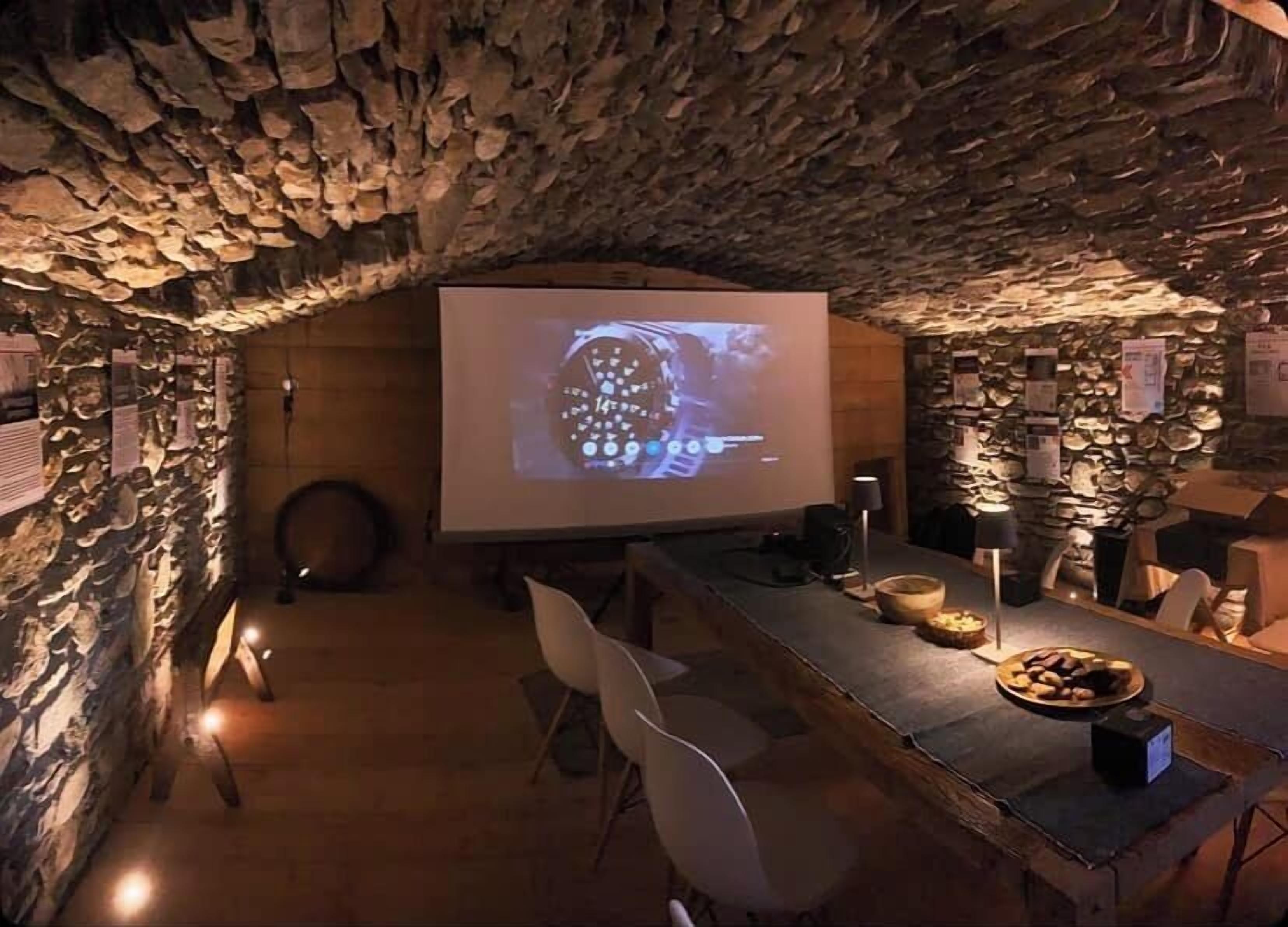 A conference room with a stone wall, a projector screen displaying a watch, and a table with snacks.