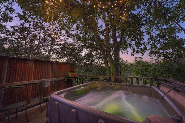 Un bain à remous doté d’une terrasse en bois et de rampes en métal, entouré d’arbres et d’une clôture en bois.