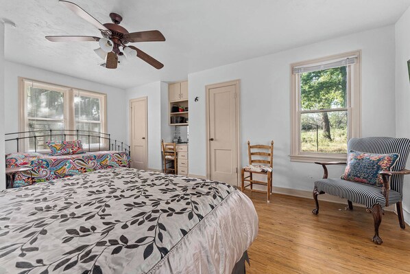 A bedroom with a bed, a chair, a desk, a ceiling fan, and a window. - E-Pies Gasthaus - Hot Tub & Near Cross Mountain! (Fredericksburg)