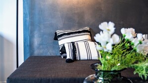 Moderni huone, jossa on tummanvärinen sohva, musta lamppu ja valkoisia kukkia sisältävä maljakko.