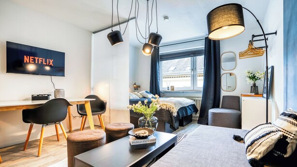 Moderni hotellihuone, jossa on sänky, työpöytä, televisio ja suuri ikkuna.