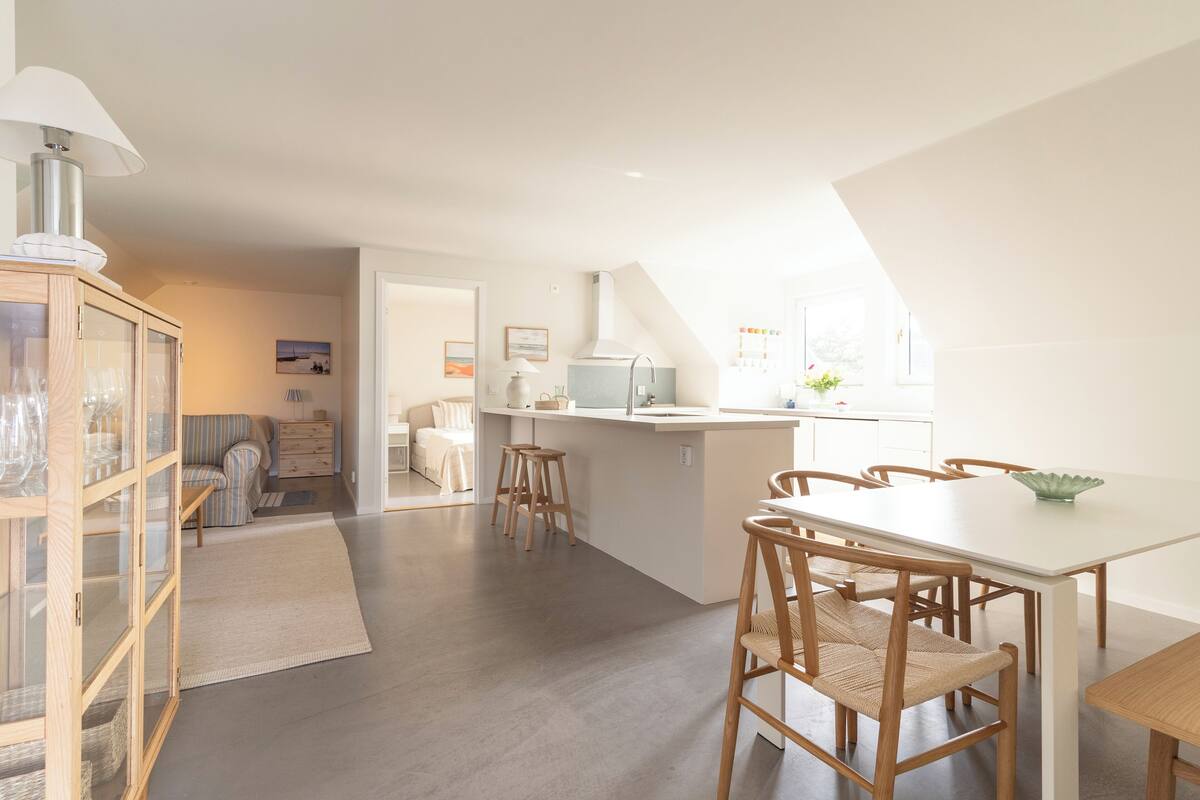 A modern kitchen with a central island, wooden chairs, and a dining table.
