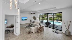 Ein modernes Wohnzimmer mit einer Couch, einem Couchtisch und Blick auf einen Swimmingpool durch große Glasfenster.