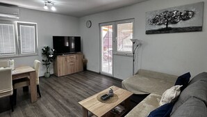 A modern living room with a sofa, coffee table, TV, and dining area. - kuća za odmor ante (selo)