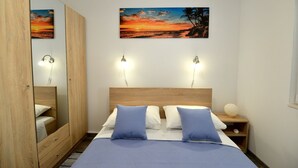 A bedroom with a wooden bed, two bedside lamps, a nightstand, a mirror, and a painting of a sunset. - kuća za odmor ante (selo)