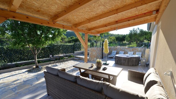 An outdoor patio with wicker furniture, a hot tub, and a stone wall backdrop. - kuća za odmor ante (selo)