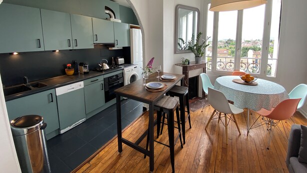 Una cocina moderna con armarios verde mar, una mesa de comedor de madera y un balcón con vistas.