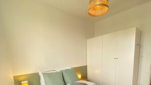 Una cama bien tendida con una manta y almohadas verdes, una lámpara de noche y un armario en una habitación con suelo de madera.