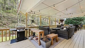 Um deck externo com churrasqueira, área de estar e vista para a floresta.