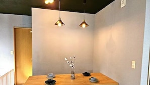 A dining area with a wooden table, two hanging pendant lights, and a vase with dried flowers. - Shima-shi kodate (Shima)