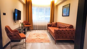 A compact living space with a sofa, two armchairs, a small table, and a TV mounted on the wall. - GARDEN'S ROOM (Edirne)