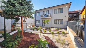 A modern two-story building with a balcony, a garden with various plants, and a clear sky. - GARDEN'S ROOM (Edirne)