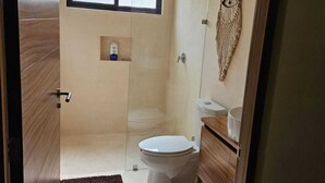 A modern bathroom with a glass shower enclosure, a toilet, and a vanity with a mirror. - Elegant 1 Bedroom - 1 bathroom Apartment (Tulum)