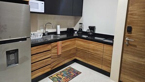 A compact kitchen with wooden cabinets, a stainless steel refrigerator, a microwave, a sink, and a coffee maker. - Elegant 1 Bedroom - 1 bathroom Apartment (Tulum)