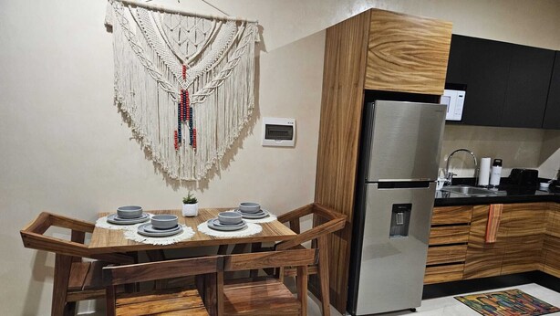 A compact kitchen with a built-in refrigerator, wooden cabinetry, and a dining area with a table set for four. - Elegant 1 Bedroom - 1 bathroom Apartment (Tulum)