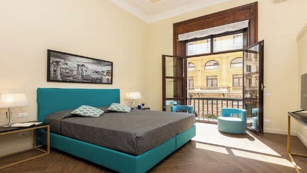 A bedroom with a bed, two bedside tables, a window with a view of a building, and a balcony with chairs. - Chic Roman Retreat: Minimalist Luxury in the Heart of Historic Rome (Roma)