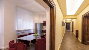 A hotel corridor with a dining area featuring a table and chairs, a radiator, and a wooden door at the end. - Chic Roman Retreat: Minimalist Luxury in the Heart of Historic Rome (Roma)