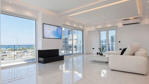 Un soggiorno moderno con ampie finestre, un divano bianco, una televisione a schermo piatto e un design minimalista.