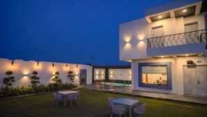 Um pátio moderno ao ar livre com piscina, área de estar e uma grande janela com vista para a piscina.