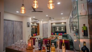 Uma área de bar com várias garrafas e copos, um sofá e um armário de vidro com garrafas.