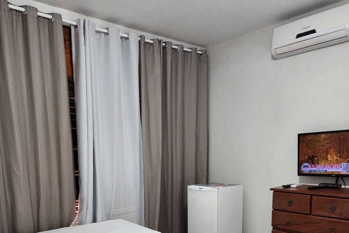 A hotel room with two beds, a wooden dresser, a television, and an air conditioning unit.