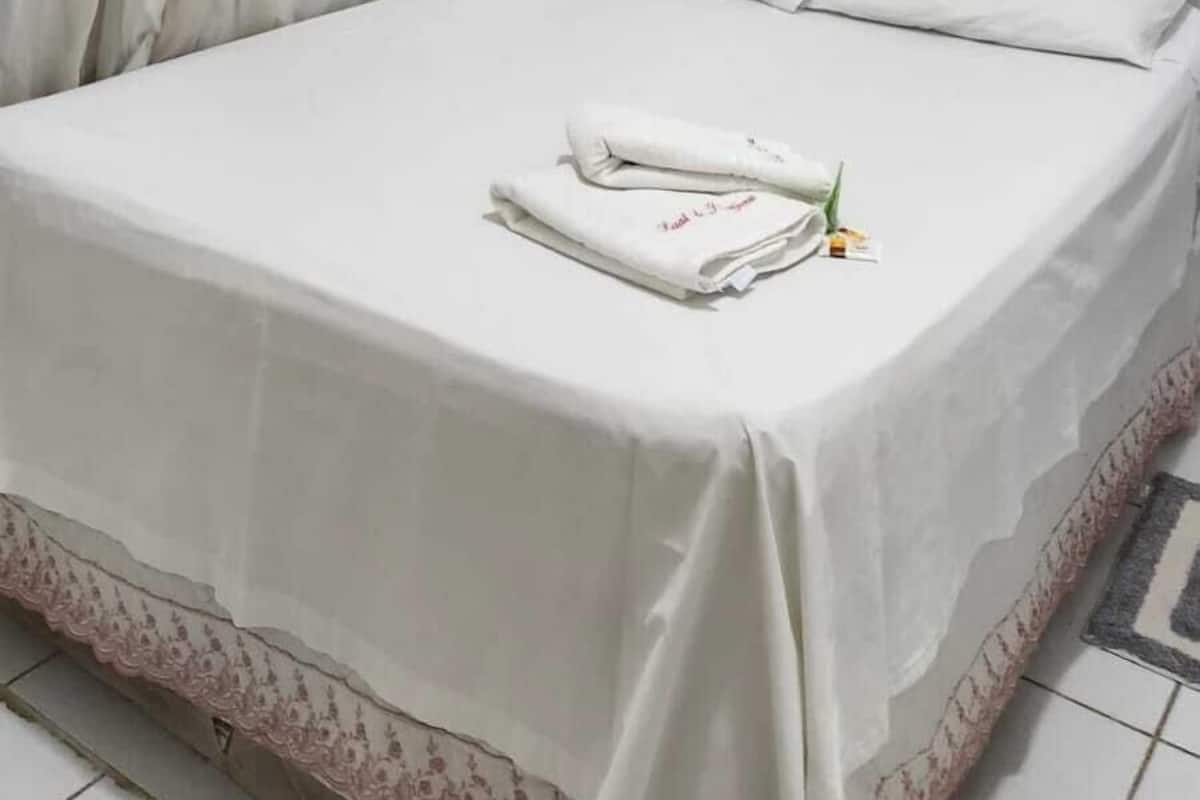 A neatly made bed with white linens and pillows, a window with white curtains, and a wall with three wooden picture frames.