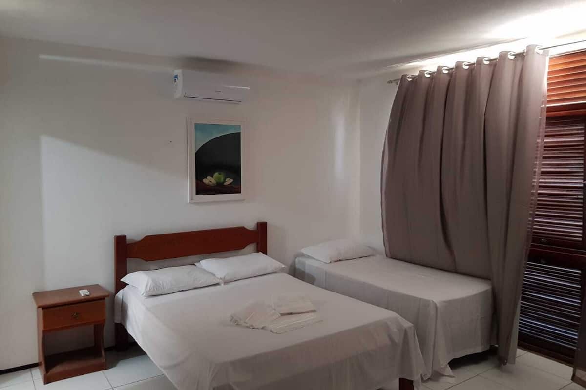 A hotel room with two beds, a nightstand, a painting on the wall, and a window with curtains.