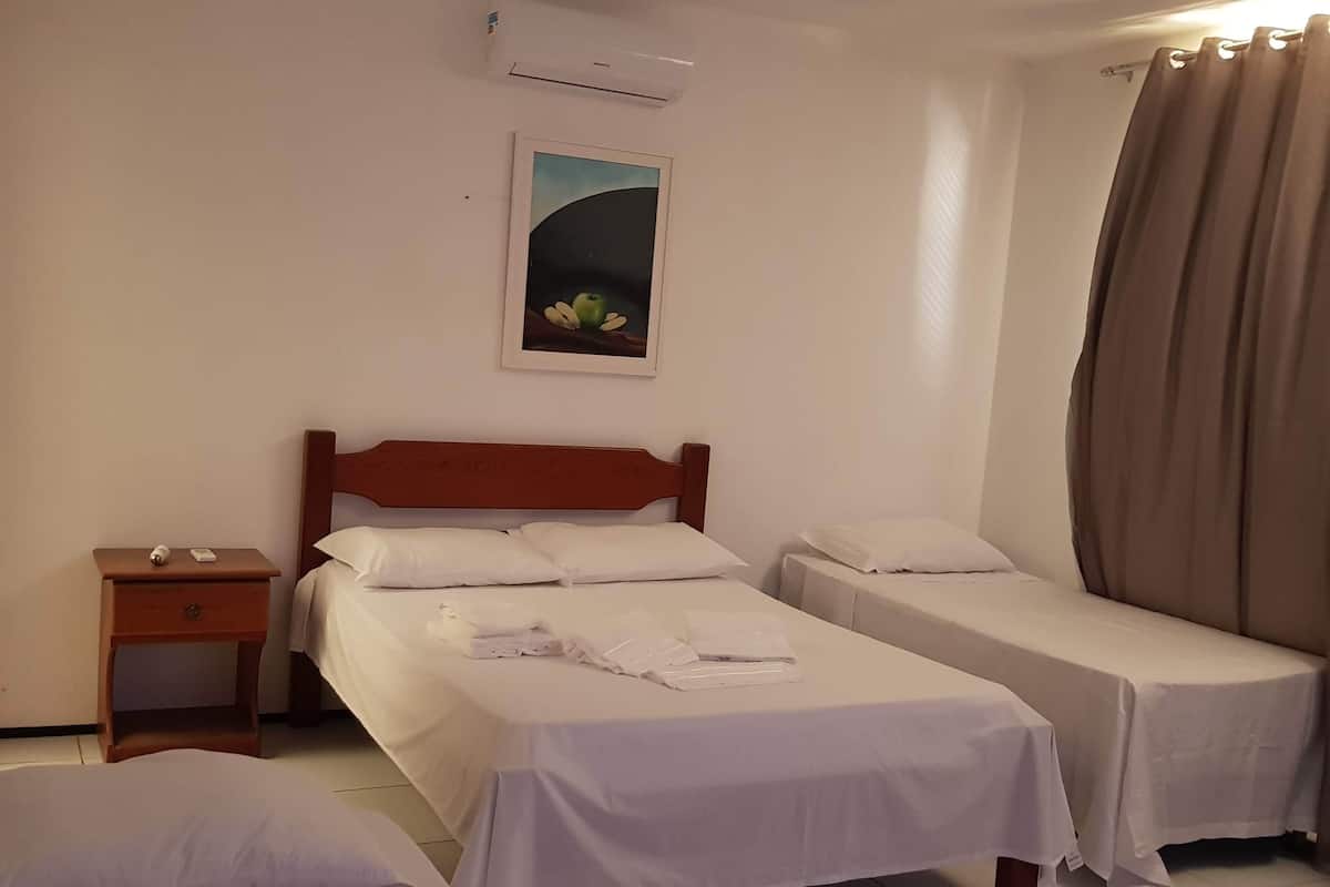 A hotel room with two single beds, a wooden nightstand, a wall-mounted air conditioner, and a painting.