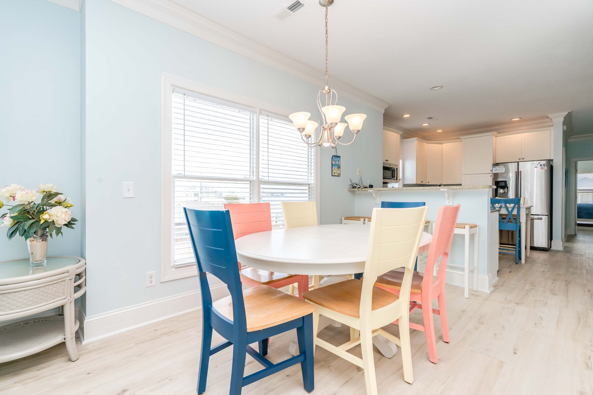 A dining area with a round table and chairs, a chandelier, and a view into the kitchen.