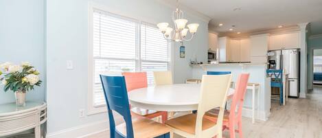 A dining area with a round table and chairs, a chandelier, and a view into the kitchen.