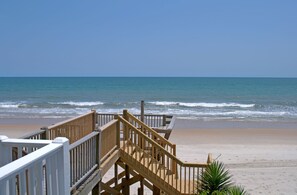 A wooden boardwalk leading to a sandy beach with the ocean in the background.