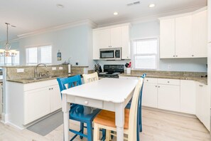 A modern kitchen with white cabinetry, a central island with seating, a microwave, and a stove.