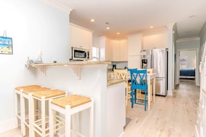 A modern kitchen with a central island, bar stools, a microwave, and a refrigerator. - Meant To Be - Oceanfront 5 BR home with elevator! (Surf City)