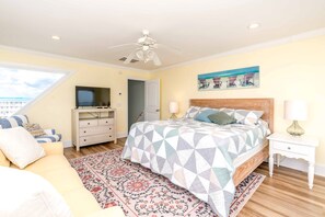 A bedroom with a bed, a television, a dresser, a nightstand, and a window with a view.