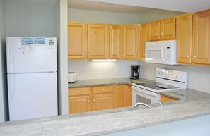 A kitchen with wooden cabinets, a white refrigerator, a microwave, a toaster, and an oven.