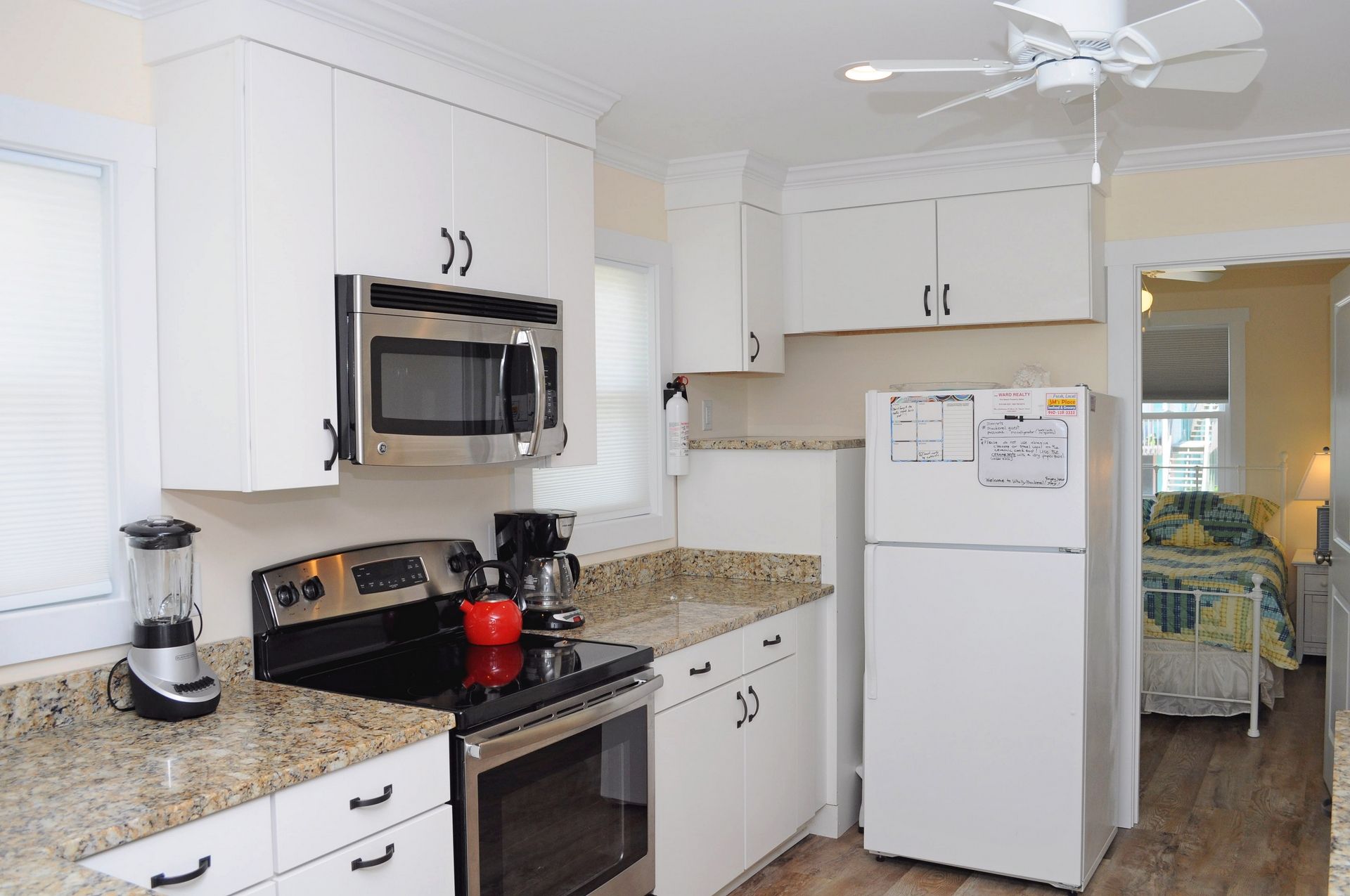 A compact kitchen with white cabinetry, a built-in microwave, a coffee maker, and a refrigerator with a note on it.