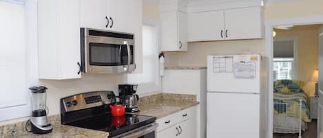 A compact kitchen with white cabinetry, a built-in microwave, a coffee maker, and a refrigerator with a note on it.