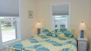 A bedroom with a bed, two bedside lamps, a window with blinds, and a picture on the wall. - Wholly Mackerel - Oceanfront, 2 Bedroom, Adorable Cottage in Surf City!  Dog (Surf City)
