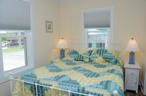 Ein Schlafzimmer mit einem Bett, zwei Nachttischlampen, einem Fenster mit Jalousien und einem Bild an der Wand.