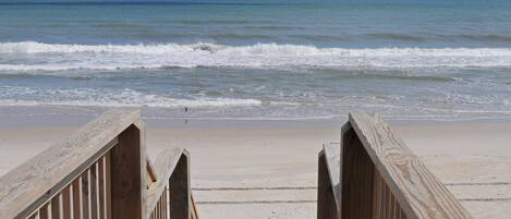 A wooden boardwalk leading to a beach with waves in the background.